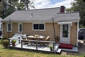 A single-story house with a porch, a dining area with outdoor furniture, and a garage. - 2 BR Cottage less than 1/2 mile to Sea Street and Glendon Beaches.  AC and Yard (Dennis)