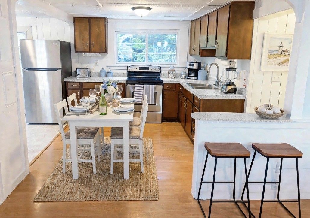 Une cuisine avec des meubles en bois, un réfrigérateur en acier inoxydable, une table à manger avec des chaises et un petit coin bar avec des tabourets.
