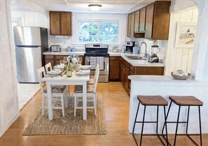 A kitchen with wooden cabinets, a stainless steel refrigerator, a dining table with chairs, and a small bar area with stools. - 2 BR Cottage less than 1/2 mile to Sea Street and Glendon Beaches.  AC and Yard (Dennis)