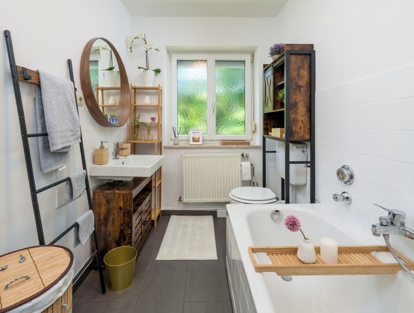 Ein modernes Badezimmer mit einem Holzbadschränkchen, einer freistehenden Badewanne, einer Toilette und einem Fenster mit Blick auf Grünflächen.
