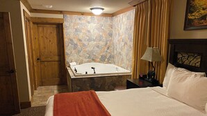 Habitación de hotel con cama, baño con bañera, puerta de madera y pared de piedra.