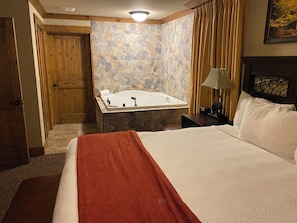 Ein Hotelzimmer mit Bett, einem Badezimmer mit Badewanne, einer Holztür und einer Steinwand.