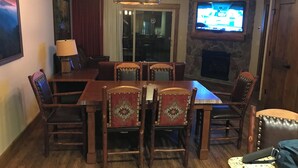 Un comedor con mesa y sillas de madera, un candelabro, un televisor y una chimenea de piedra.