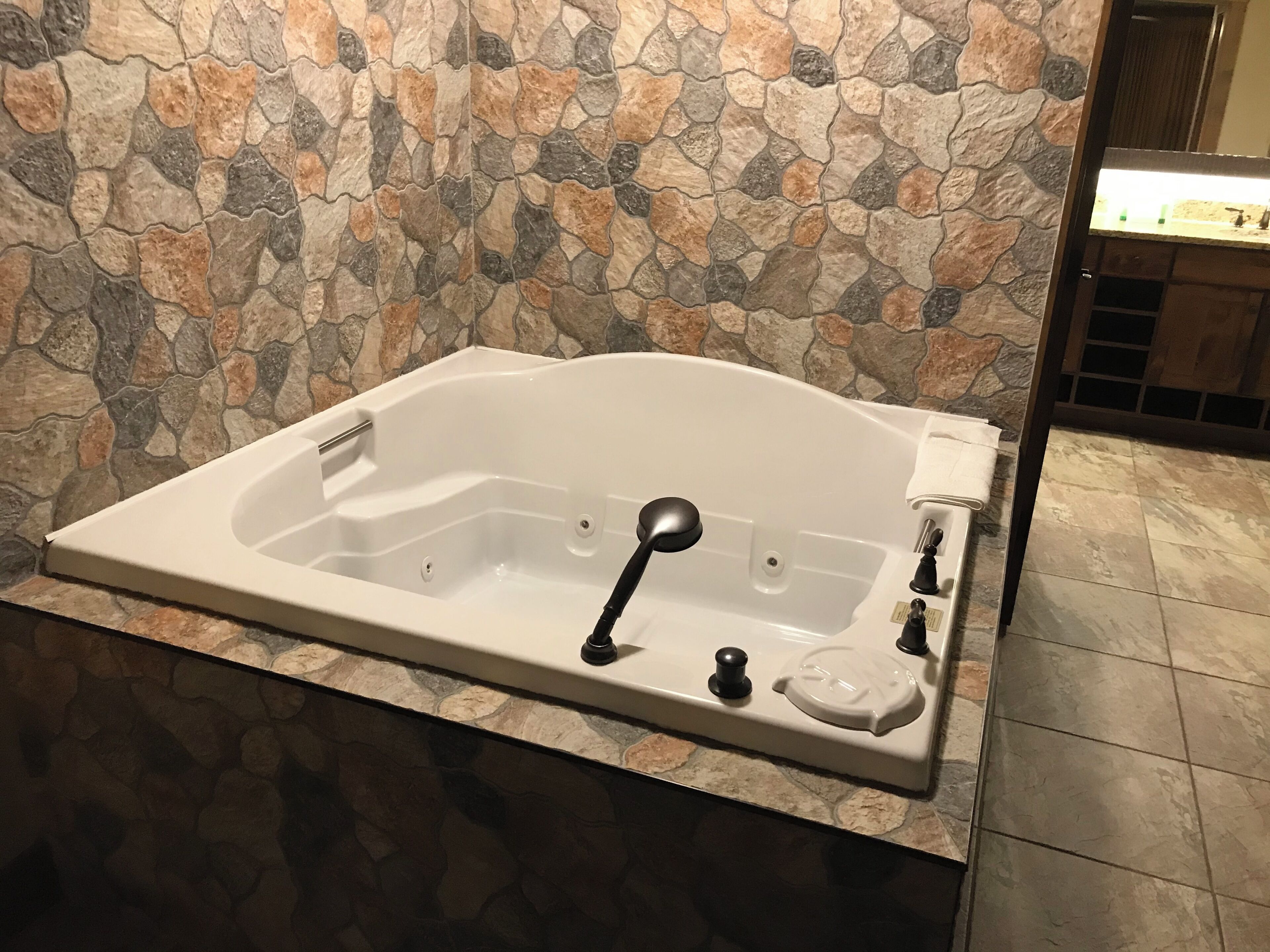 Une baignoire blanche, dotée de robinetterie noire, placée devant un mur en pierre.