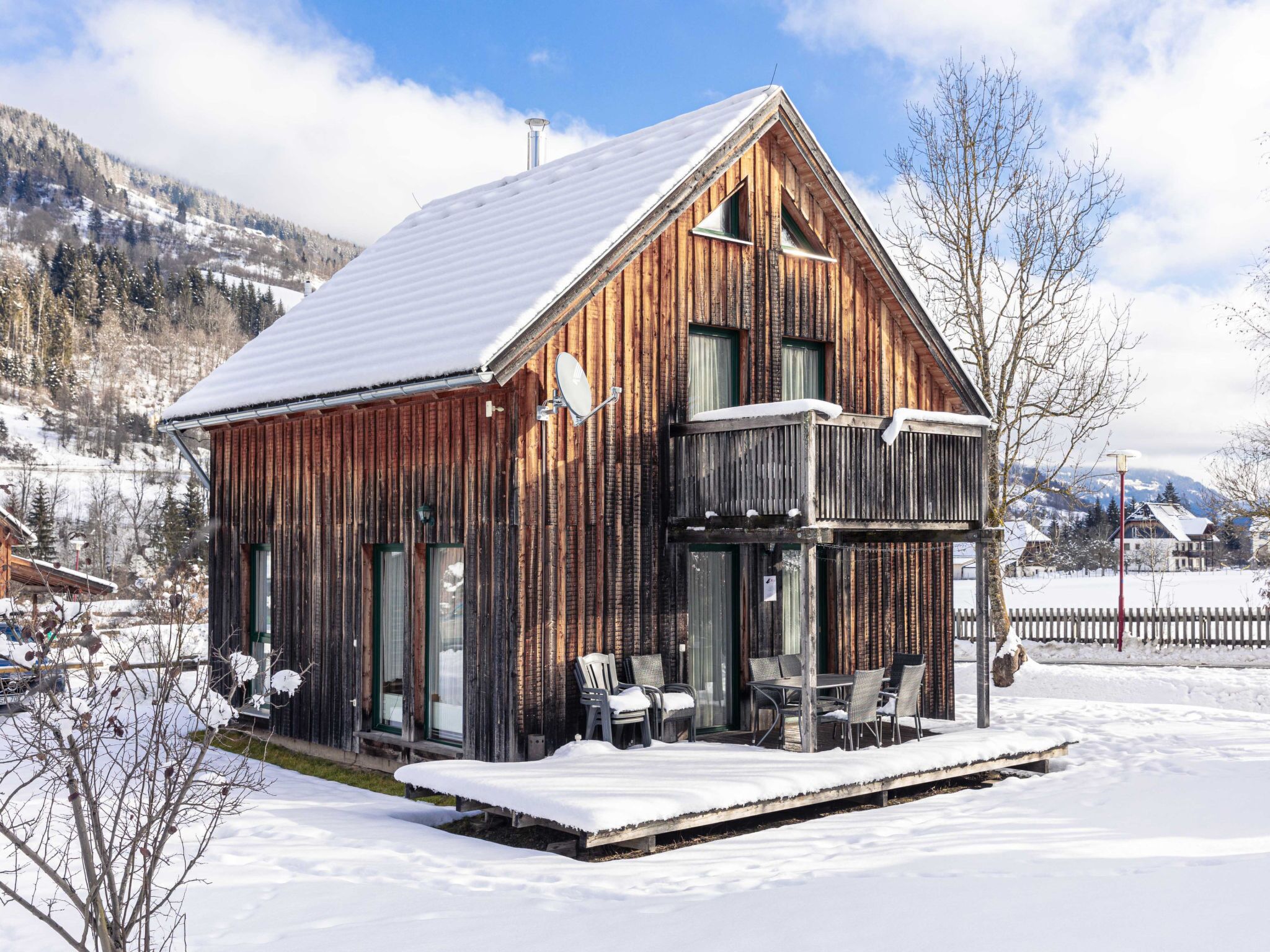 A wooden cabin with a balcony, snow-covered surroundings, and a mountainous backdrop.
