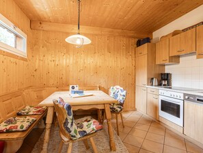 Puisesti sisustettu tila, jossa on ruokapöytä, tuoleja, riippuvalaisin sekä keittiöalue, jossa on kaappeja ja kodinkoneita.