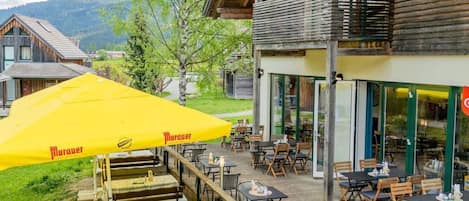 A wooden building with a balcony, outdoor seating, and a yellow umbrella.