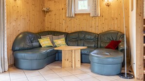 Una habitación acogedora con un sofá de cuero curvo, una mesa de centro de madera y dos lámparas fijadas a la pared.