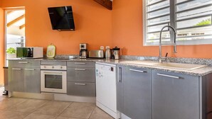 A modern kitchen with grey cabinets, a built-in oven, a microwave, a coffee maker, and a sink. - Villa Ti'Twoine - Sea view - Sunsets - (Pointe-Noire)