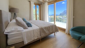 A bedroom with a bed, a chair, a lamp, and a balcony with a view. - An oasis in the middle of nature (Pollença)