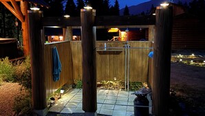 Un espace de douche extérieur en bois, doté d’un sol en pierre, entouré d’une clôture en bois, avec une vue sur les montagnes en arrière-plan.