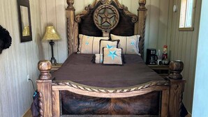 Une chambre à coucher avec un plafond en bois, un ventilateur de plafond, un grand lit doté d’une tête de lit décorative et une table de chevet avec une lampe.