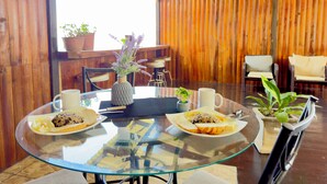 A dining area with a glass table, two plates of food, a vase with flowers, and wooden walls. - Paulos View Lodge (Venecia)