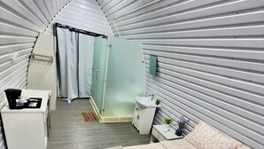 A compact, modern room with a bed, a small bedside table, a mirror, a sink, and a shower area. - Paulos View Lodge (Venecia)