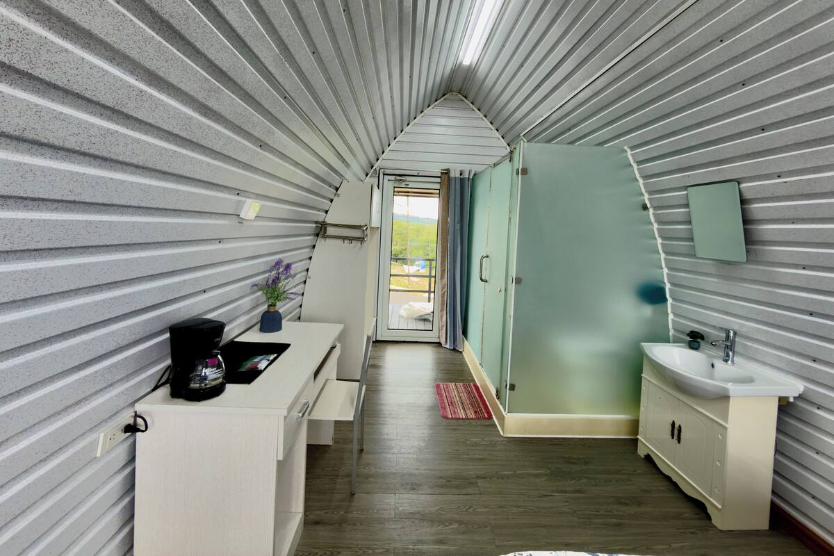 A narrow hallway with a sloped ceiling, a sink, a mirror, and a door leading outside.