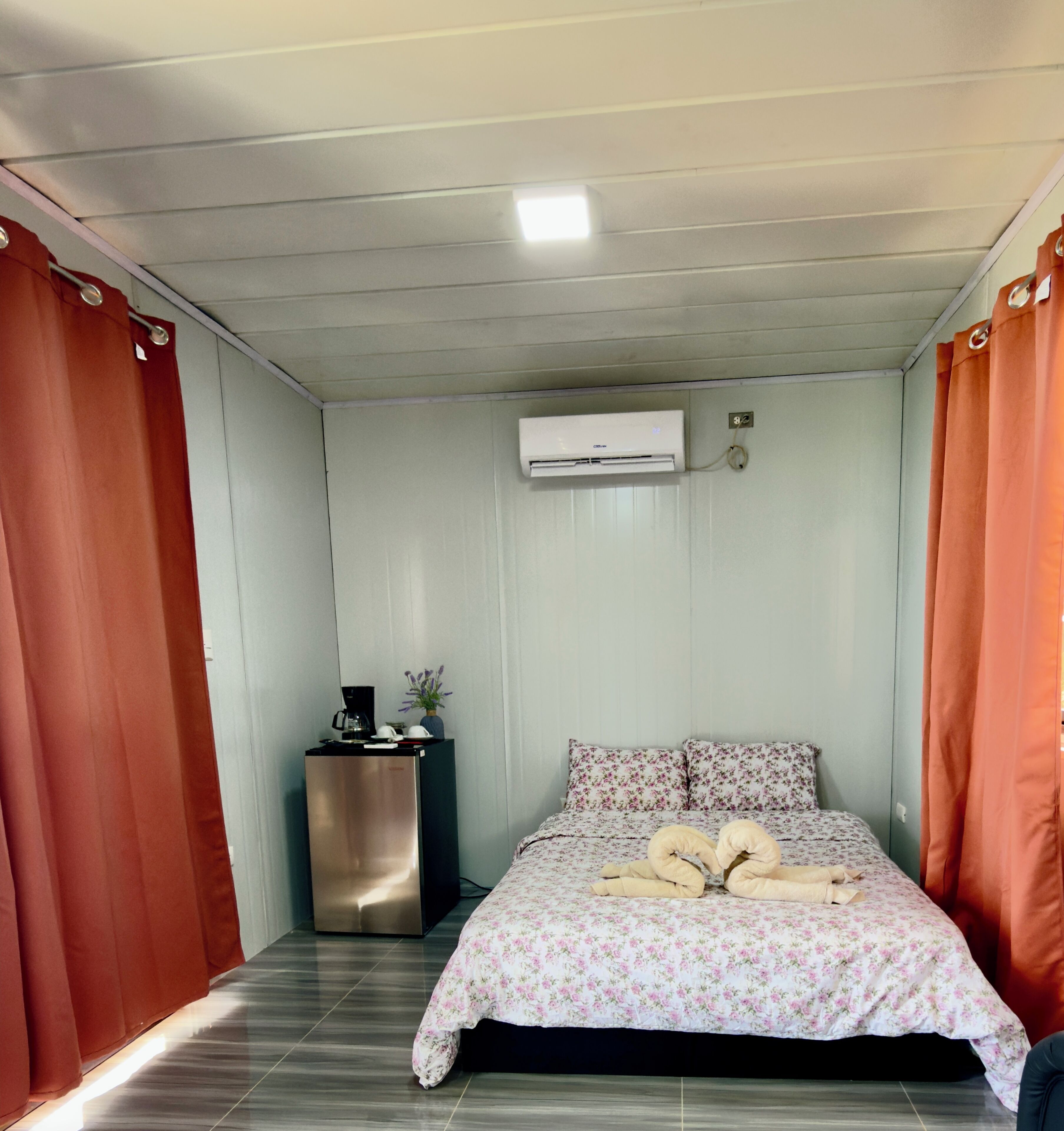 Une chambre avec un lit, une petite table avec une bouilloire et un climatiseur fixé au mur.