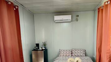 Une chambre avec un lit, une petite table avec une bouilloire et un climatiseur fixé au mur.