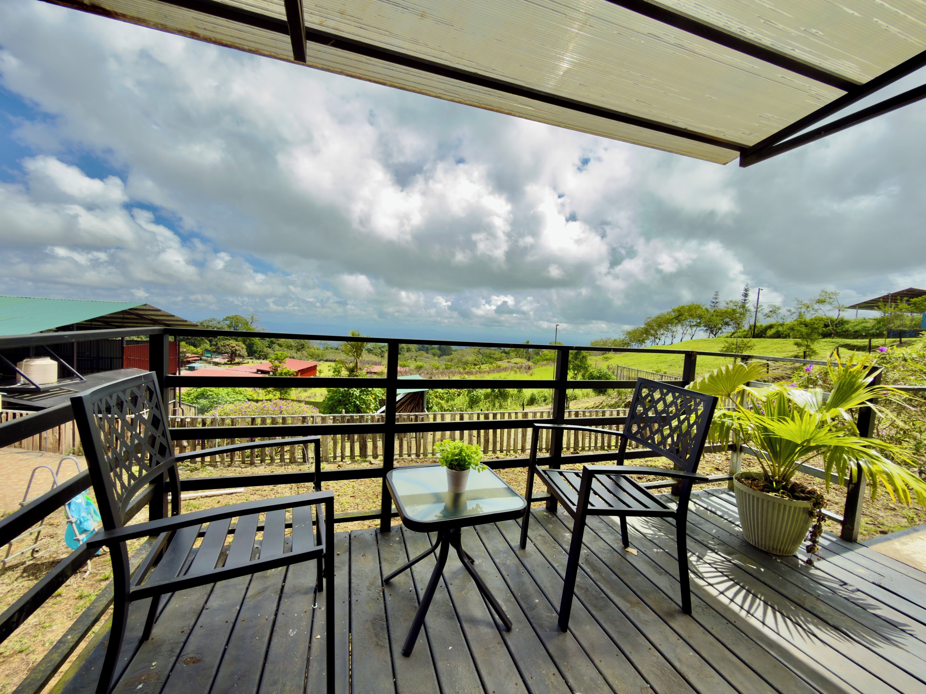 A wooden deck with a glass table and chairs, overlooking a green landscape with houses.