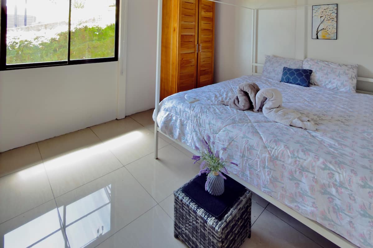 A bedroom with a bed, a window, a wardrobe, and a small table with a vase.