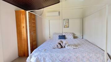 Une chambre à coucher avec un lit, une armoire en bois, un petit tabouret en osier et un ventilateur de plafond.