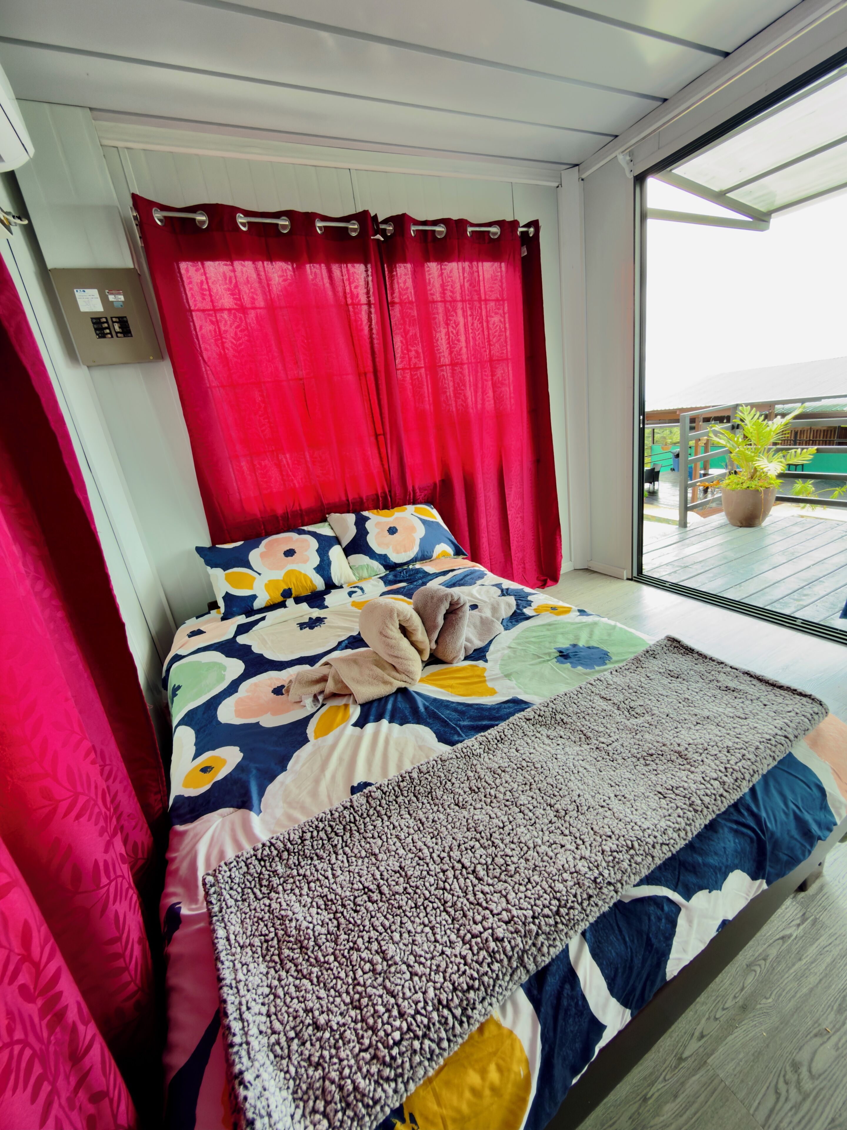 Una habitación con cama, cortinas rojas, un ventanal y una planta en maceta.