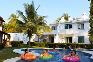A swimming pool with inflatable rings, palm trees, and a white building with a dome. - Casa Coral (Manzanillo)