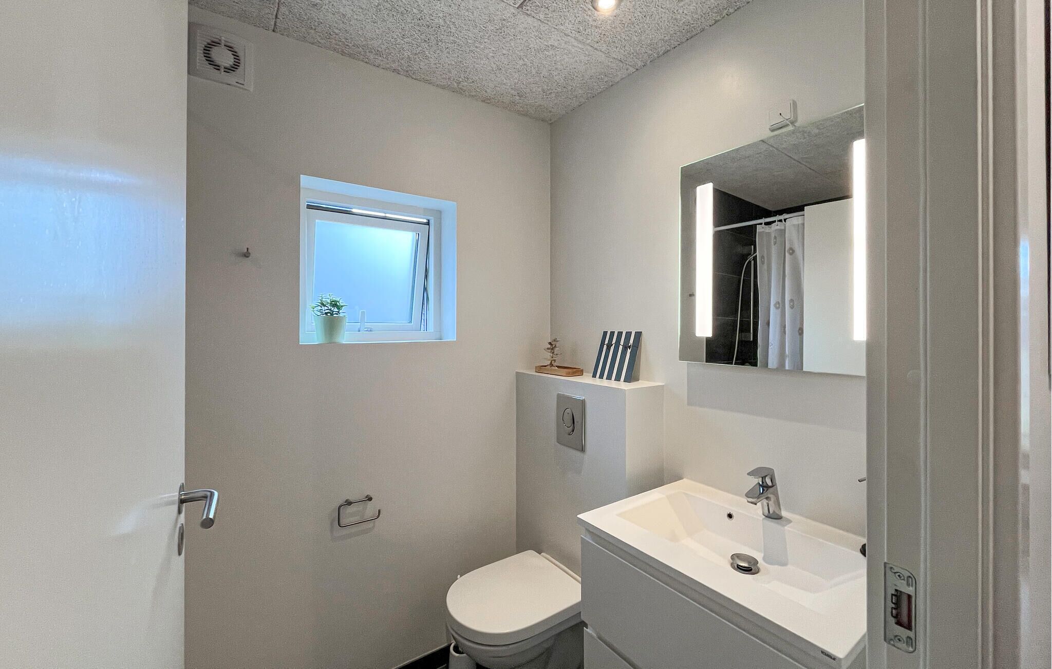 Un baño pequeño con inodoro, lavamanos, espejo y un ventanal.