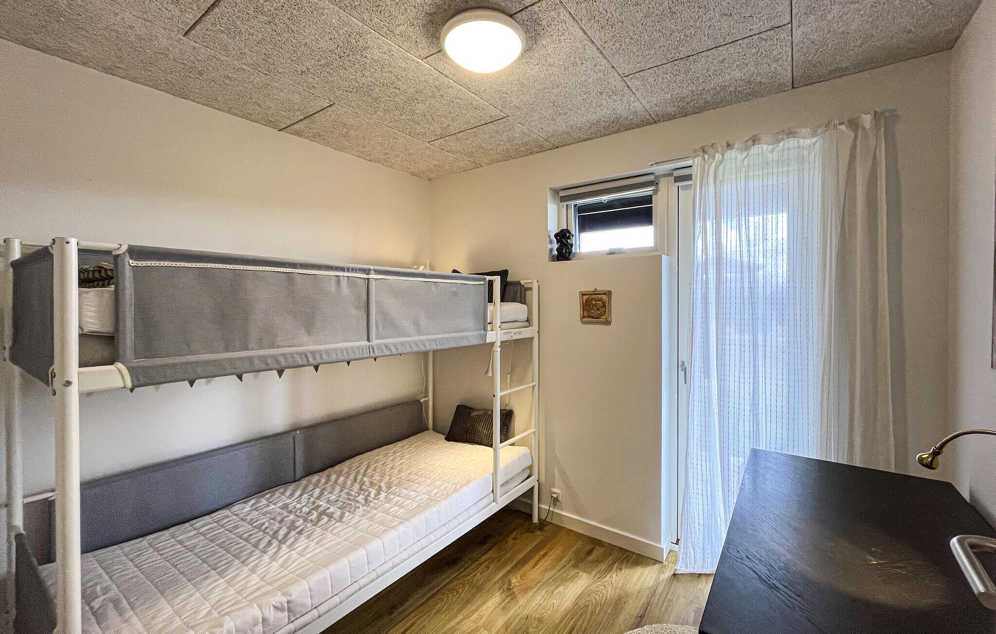 A bunk bed room with a window, a desk, and a small picture on the wall.