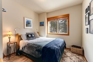 A bedroom with a bed, a window, a lamp, and framed pictures on the wall.