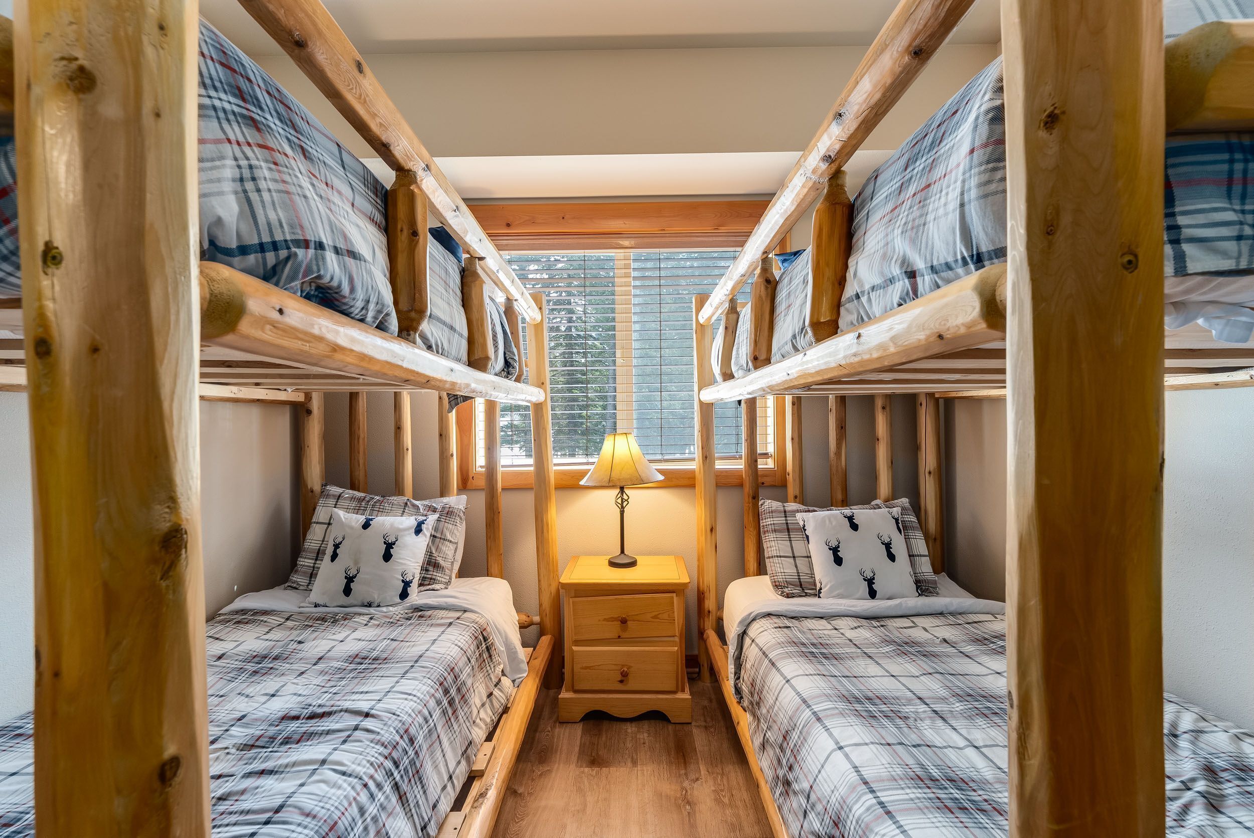 A room with two bunk beds, a bedside table with a lamp, and a window with blinds.