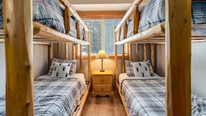 Una habitación con dos literas, una mesita de noche con lámpara y una ventana con persianas.