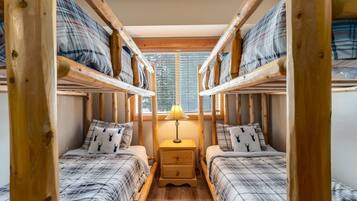 A room with two bunk beds, a bedside table with a lamp, and a window with blinds.