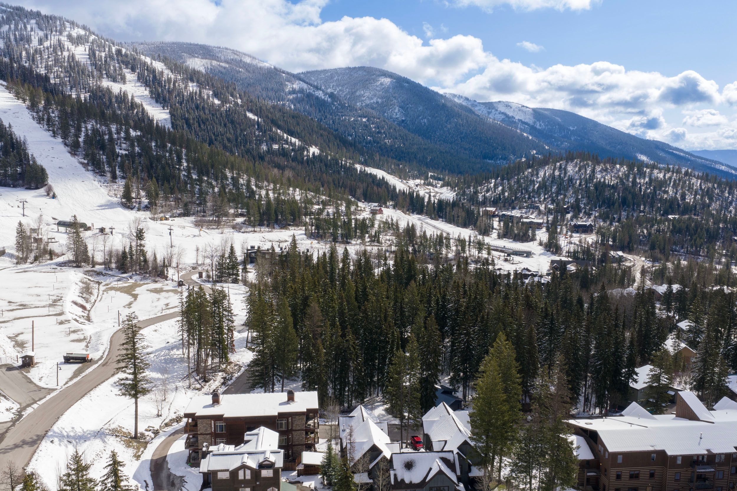 A mountain lodge with multiple buildings, a ski slope, and surrounding forested mountains.