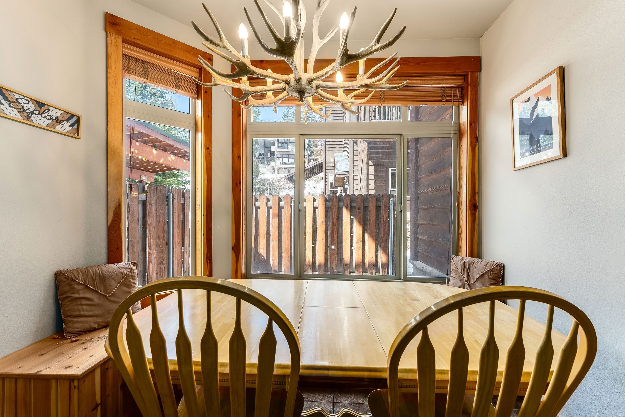 A dining area with a wooden table and chairs, a chandelier, and a large window with a view of buildings outside.