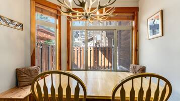 A dining area with a wooden table and chairs, a chandelier, and a large window with a view of buildings outside.