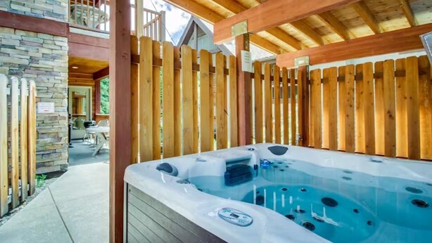 Un jacuzzi bajo una terraza de madera con paredes de piedra y un balcón.