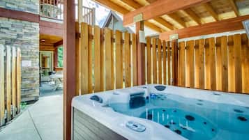 A hot tub under a wooden deck with stone walls and a balcony.