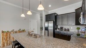 Una cocina con encimeras de granito, electrodomésticos de acero inoxidable, iluminación colgante y armarios oscuros.