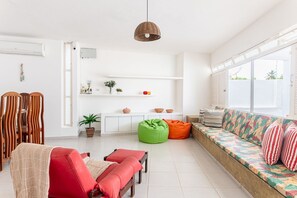 Ein helles Wohnzimmer mit einer Couch, Sesseln, einer Pendelleuchte und einem Fenster.
