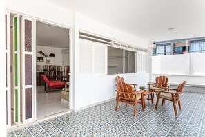 Ein Zimmer mit Fliesenboden, einem Esstisch mit Stühlen, einem roten Sofa und einem Fenster mit Jalousien.
