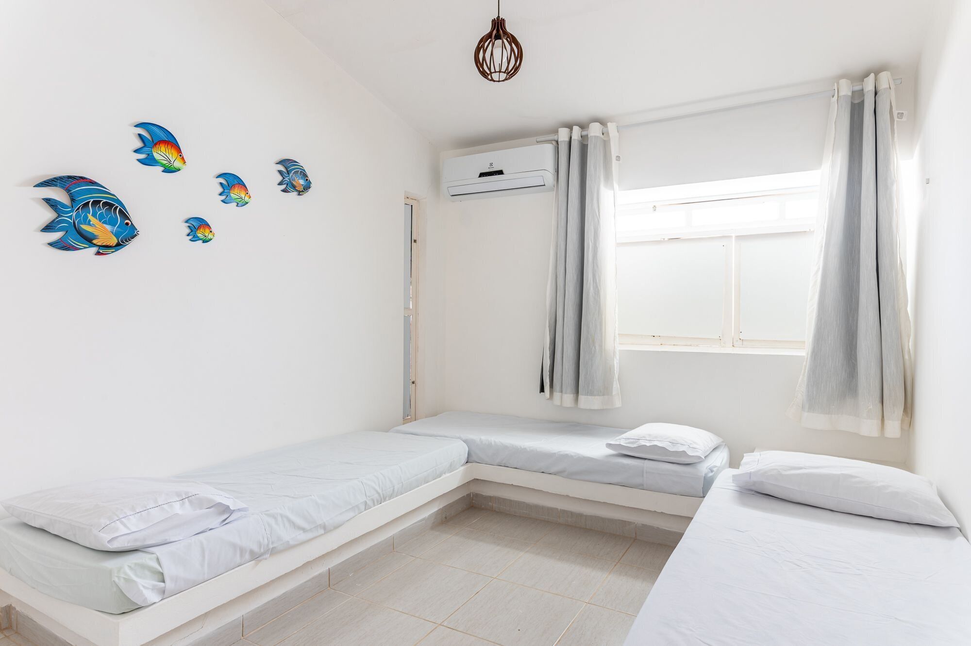 Un dormitorio con dos camas, una ventana con cortinas, un equipo de aire acondicionado y decoración en la pared.
