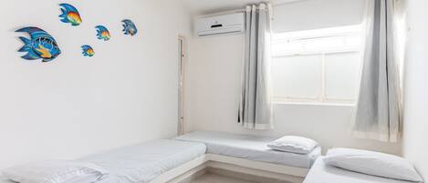 Un dormitorio con dos camas, una ventana con cortinas, un equipo de aire acondicionado y decoración en la pared.