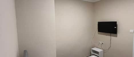 Una cama individual con colcha a rayas, una almohada blanca, un televisor de pantalla plana montado en la pared y una mesita de noche con toma de corriente.