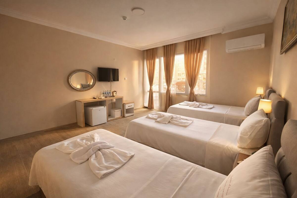 A hotel room with two beds, a desk with a TV, and a window with curtains.