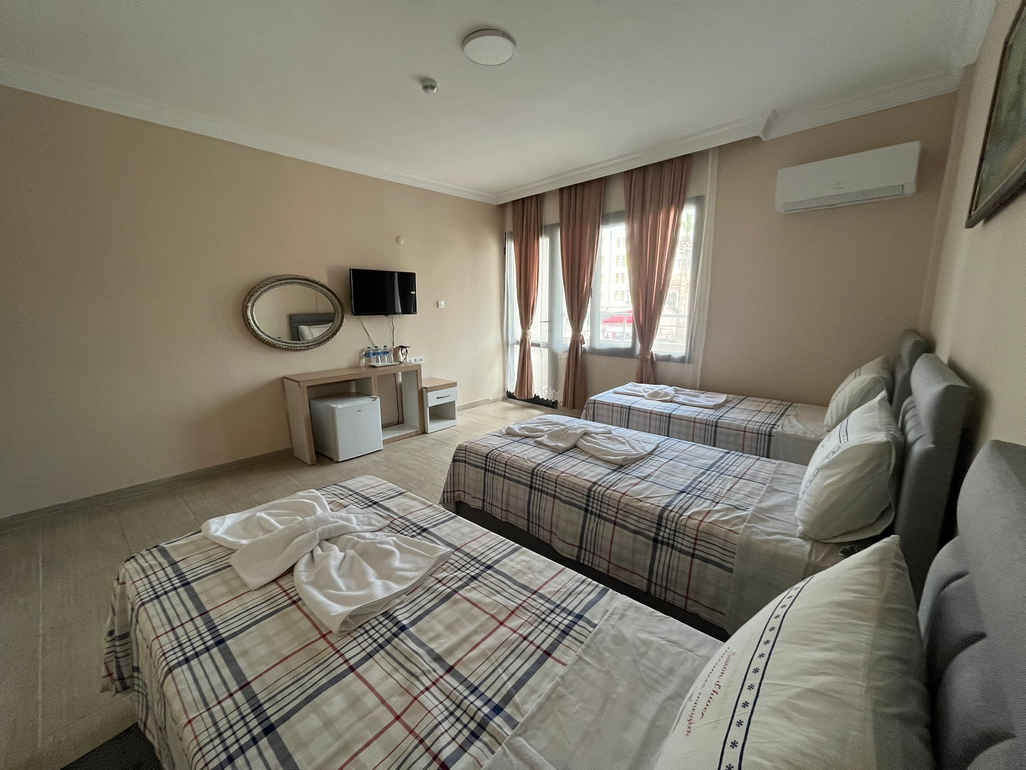 Habitación de hotel con dos camas, un escritorio, un televisor y una ventana con cortinas.