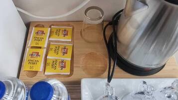 Una cuina amb un taulell, una tetera, ampolles d'aigua, un got i sobres de cafè soluble.