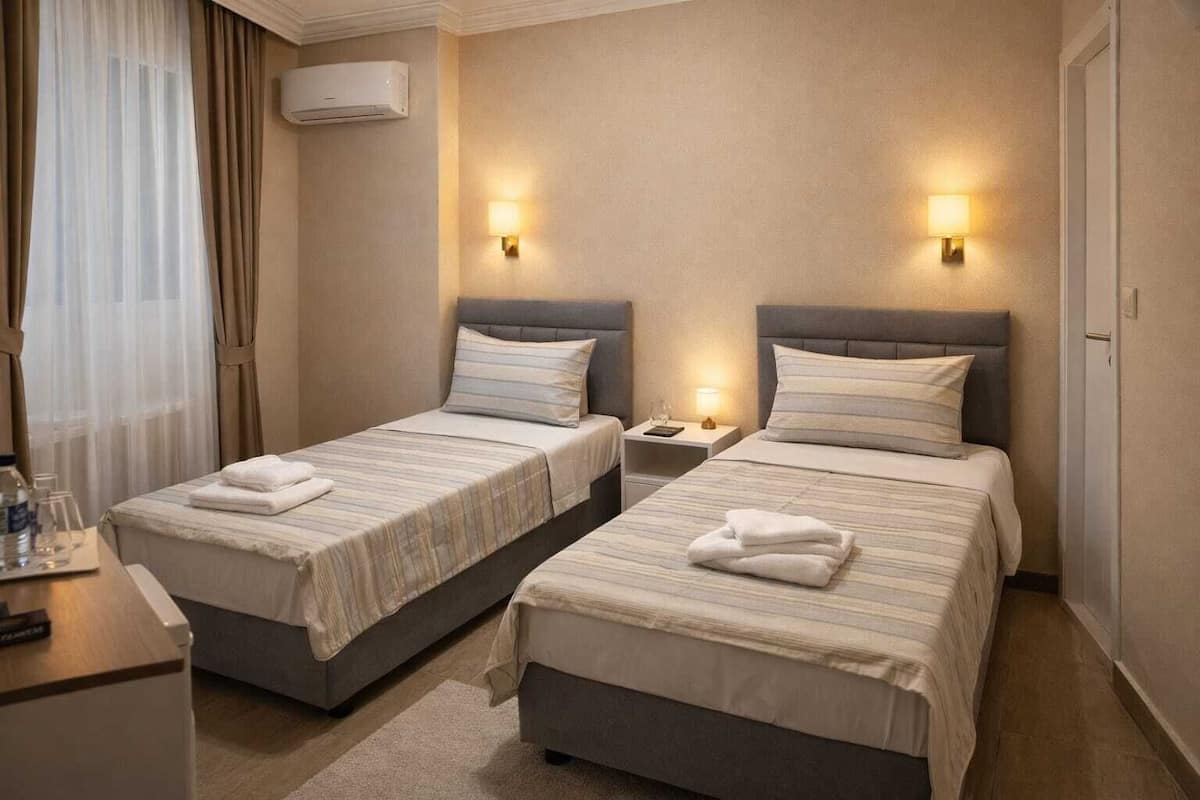 A hotel room with two beds, a bedside table with a lamp, and an air conditioning unit.