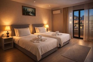 Habitación de hotel con dos camas, un cuadro en la pared, un equipo de aire acondicionado y vistas a través de un ventanal.
