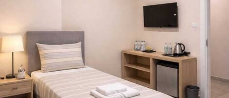 Habitación de hotel ordenada con cama, mesita de noche, lámpara, televisor, escritorio y un pequeño cubo de basura.