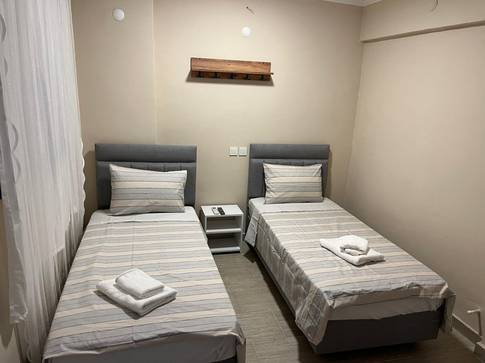 A twin room with two beds, a wooden shelf above, and a small bedside table with a phone.